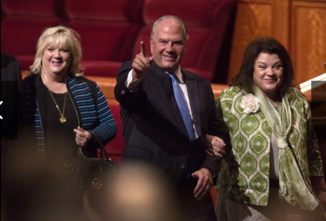 photo d'Elder Rasband, membre du collège des 12 apôtres au bras de son épouse quittant le centre de conférence générale en saluant la congrégation.